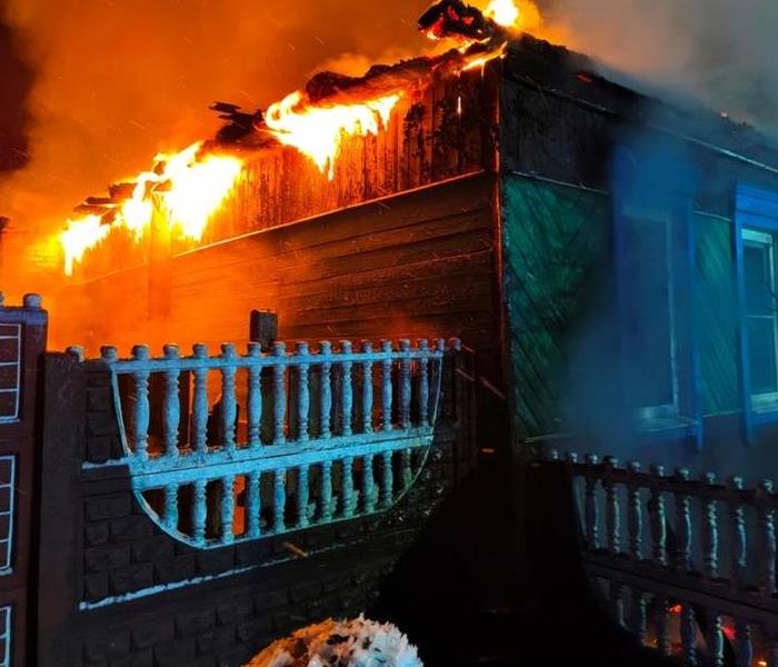 A closeup of a residential home with its roof on fire during the evening.